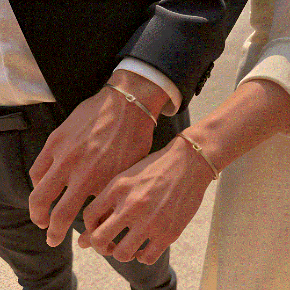 Two people holding hands with gold bracelets on a blurred background